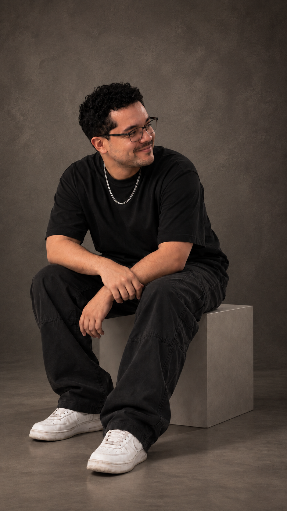 Retrato de ARYUN sentado em um cubo, usando roupa preta oversized